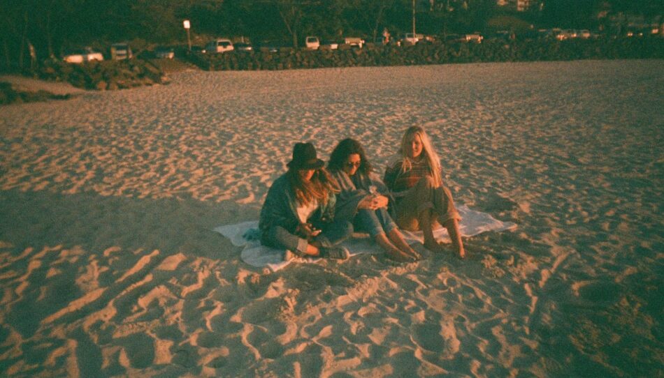 Three women spontaneously sitting on a blanket on the beach.