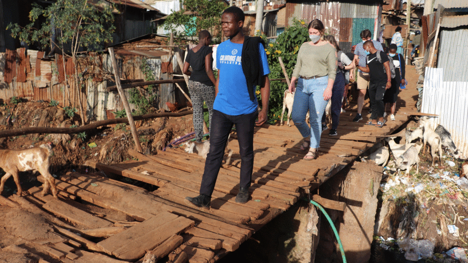 A group of people, with a mirror of hope in hand, bravely walking across a wooden bridge in a slum.