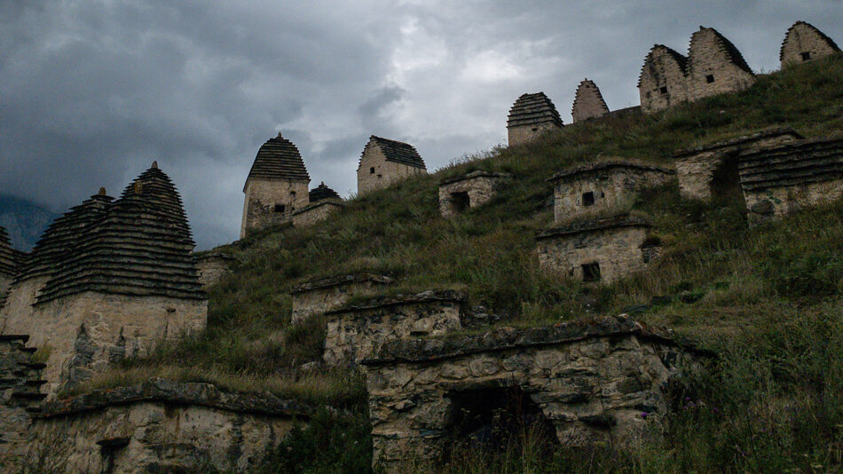 A group of stone buildings on a hillside under a cloudy sky.