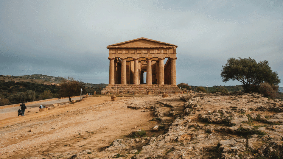 Looking for things to do in Sicily? Explore a mesmerizing temple nestled in a rocky area, surrounded by a picturesque cloudy sky.