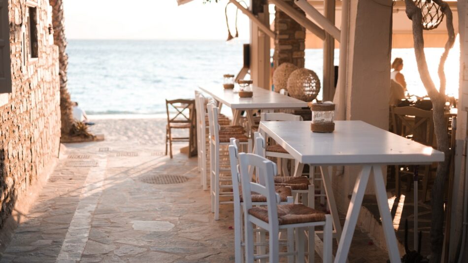 A beach bar with white tables and chairs located in one of the best beaches in Greece.