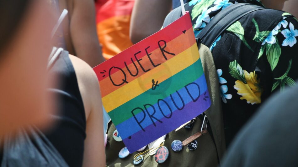 A group of people holding a sign that says queer is proud.