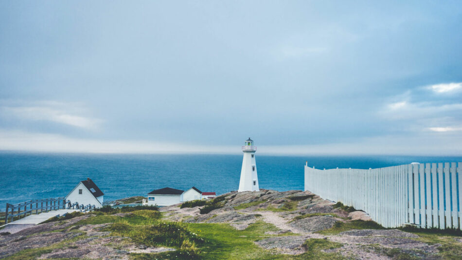 A lighthouse sits on top of a hill overlooking the ocean.