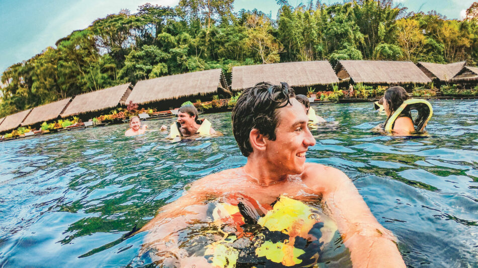 A group of people swimming in the water near a hut, enjoying one of the most beautiful destinations in Thailand.