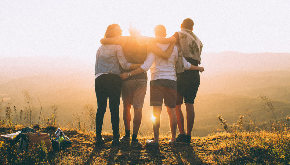 A group of friends standing on top of a mountain at sunset.