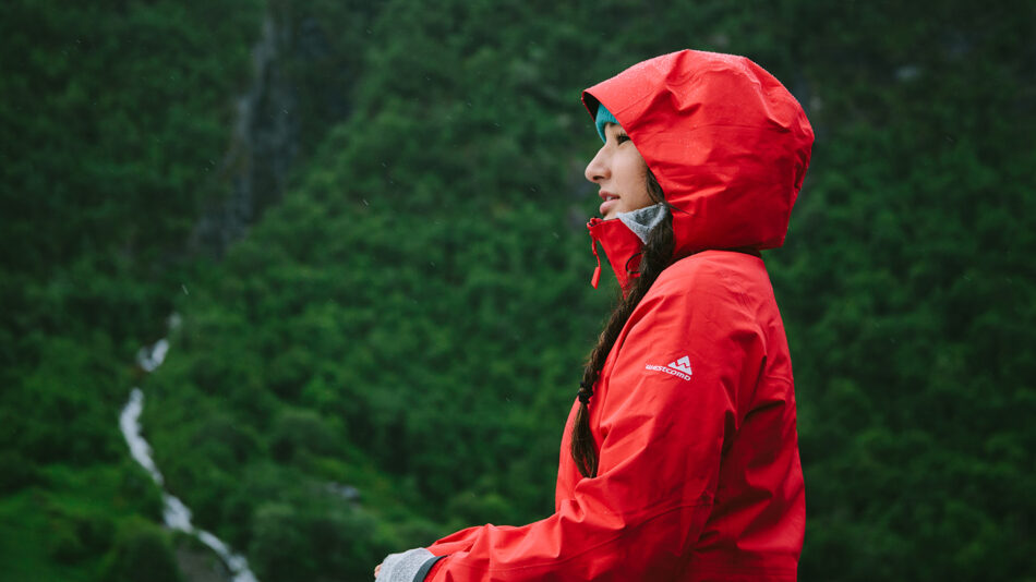 A woman in a red jacket enjoying Japanese forest bathing near a waterfall.