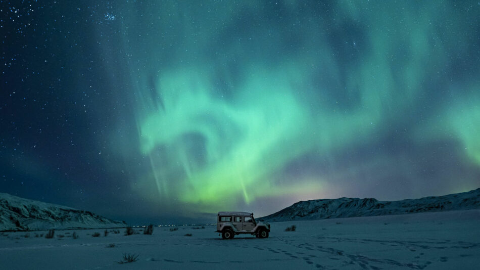 The aurora borealis illuminates a jeep amidst the snowy landscape, creating a captivating scene for travel photography enthusiasts.