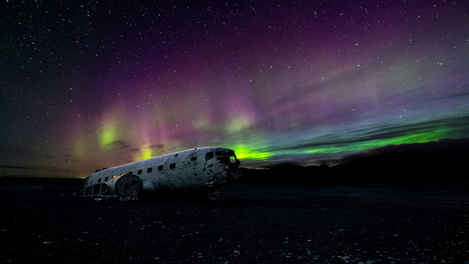 A captivating travel bucket list experience - witnessing an old plane beneath the mesmerizing aurora borealis in Iceland.