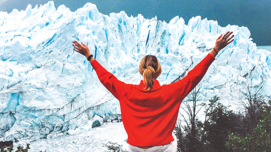 A woman standing in front of a glacier in Patagonia with her arms outstretched.