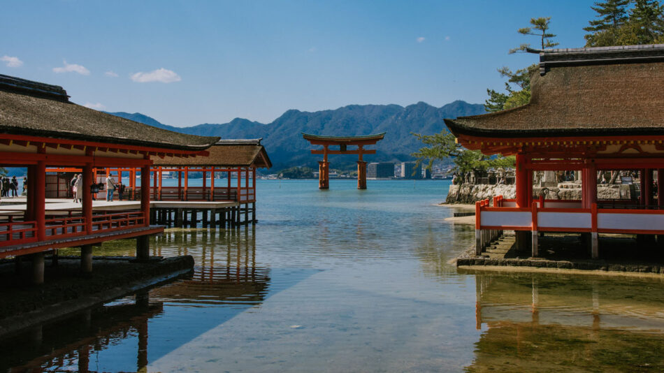 A red tori tori gate on the shore of a body of water in Japan.