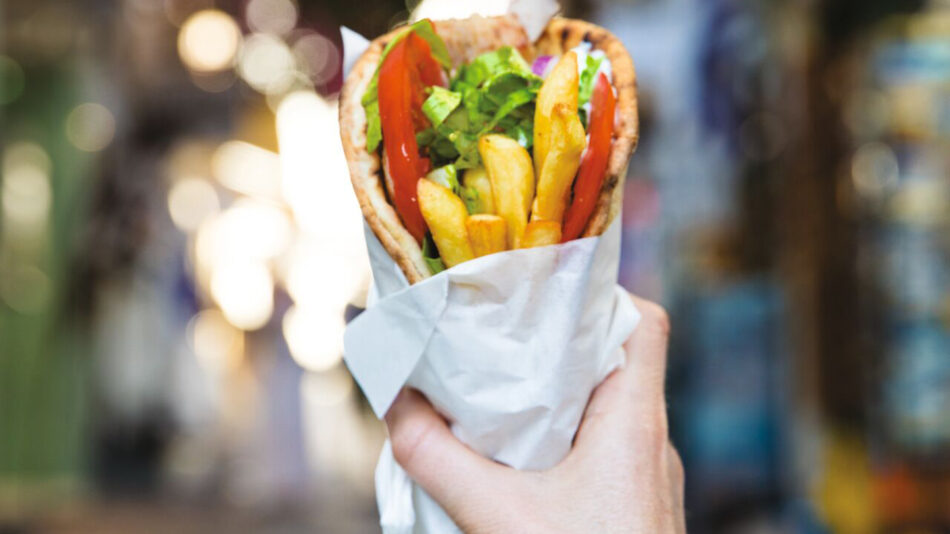 A person is holding a sandwich in a paper wrap.