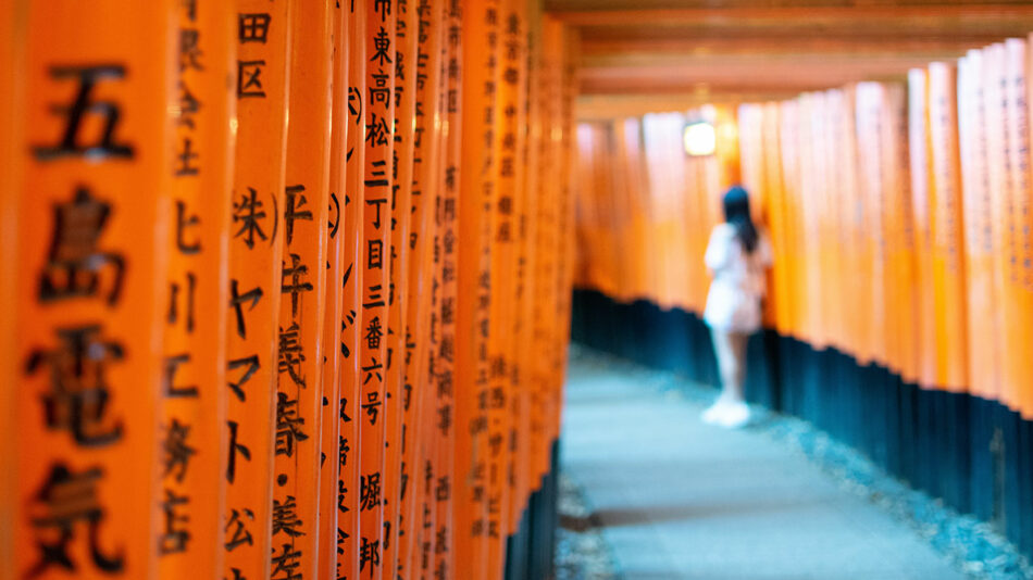 A woman is walking down a hallway of orange tori tori featured in Condé Nast Traveller.