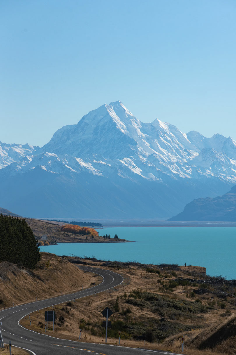 A serene road leading to a lake with snow capped mountains in the background, offering solace for solo travelers after a breakup.