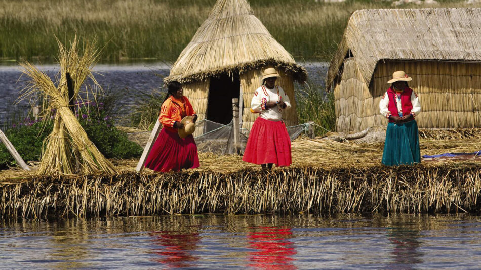 Three women standing in front of a hut near Lake Titicaca.