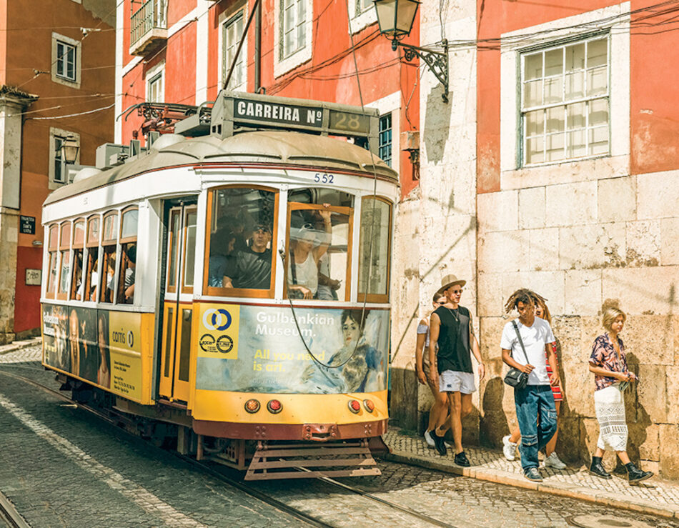 A group of people standing next to a tram on a street in Lisbon, one of the top things to do in Portugal.