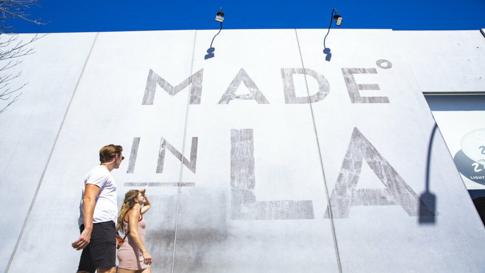 Two people walking past a building that says made in la.