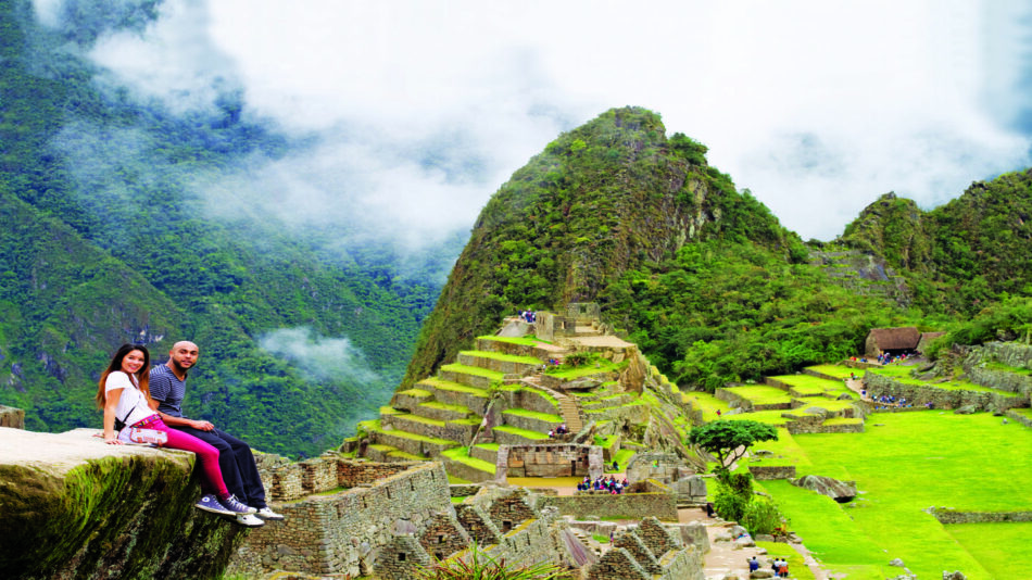 Two people sitting on a ledge admiring the breathtaking view of Machu Picchu, one of the best places to visit in Latin America.