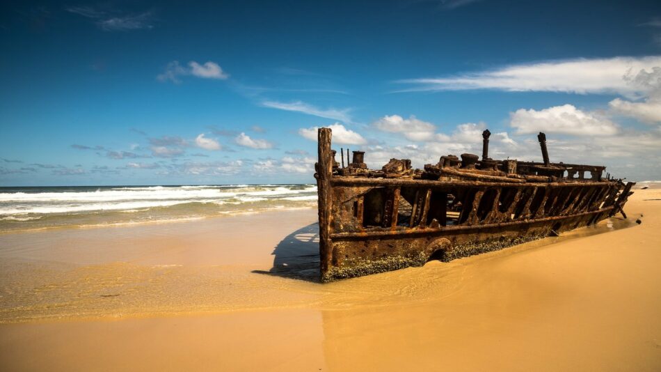 A rusty ship sits on a sandy beach.