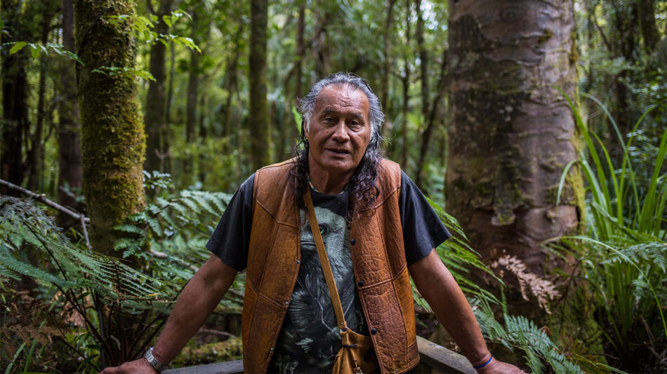 A man performing a Maori war dance in the middle of a forest.