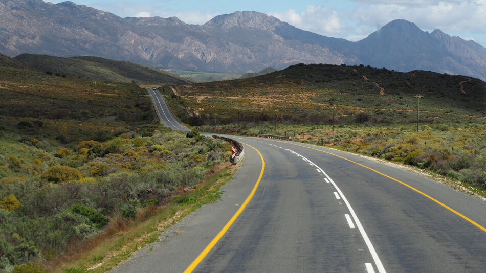 One of the best places to visit in South Africa is a road surrounded by majestic mountains in the background.