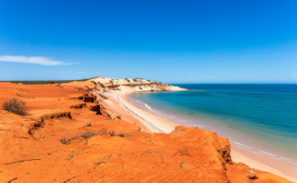 A beach with red sand and a blue sky.