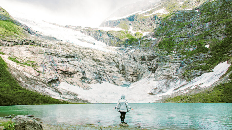 An instagrammable snowy destination with a person standing in front of a mountain and a lake in the background.