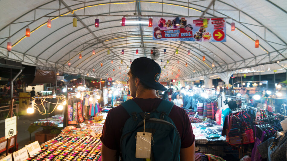 A man with a backpack exploring a market in Chiang Mai.