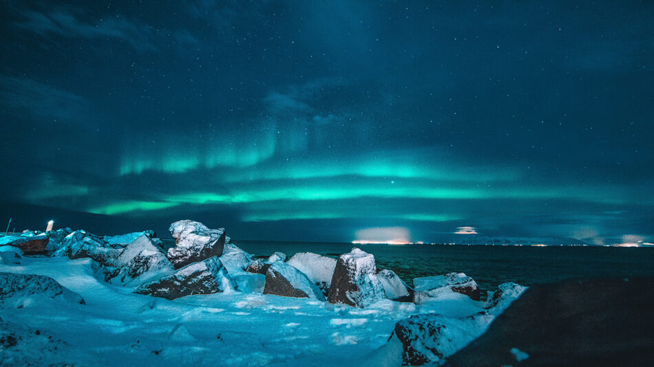 The aurora borealis lights up the sky over a rocky shore.