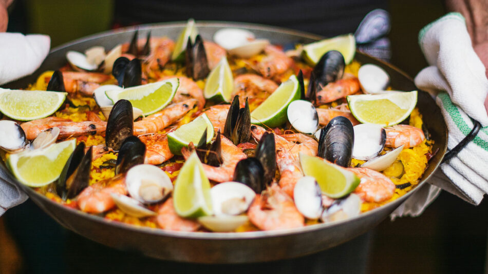 A man is holding a pan full of seafood and shrimp.