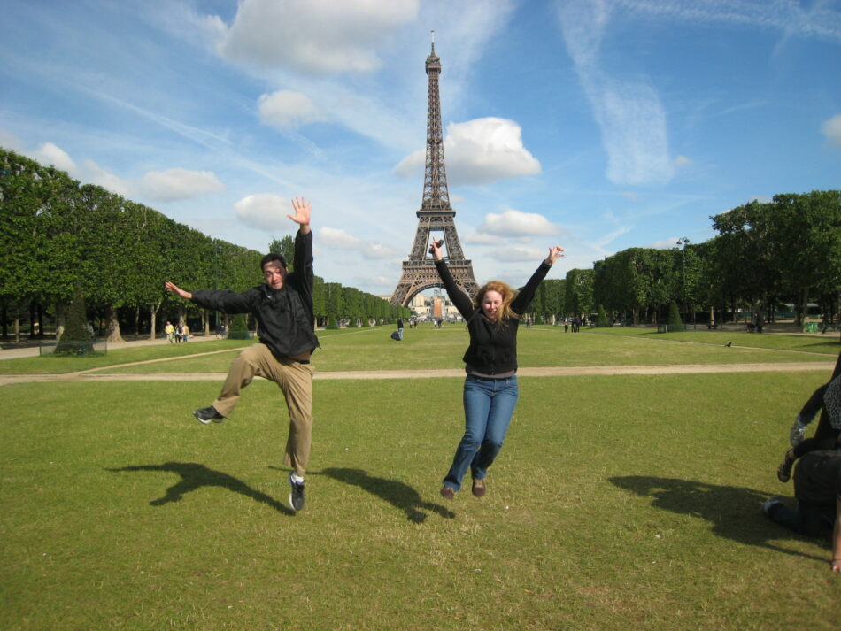 A man and a woman enthusiastically jumping in the air while traveling around the world.