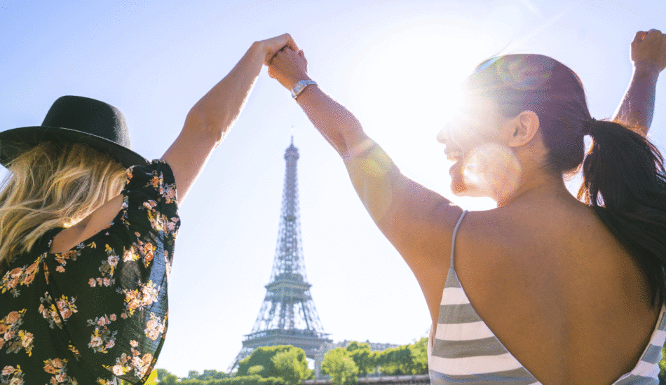 Two women raising their hands in front of the Eiffel Tower during a Contiki adventure.