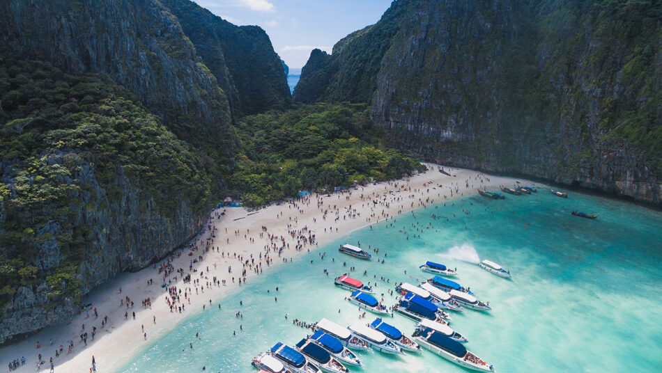 A group of boats parked on a beach near a cliff, one of the 10 places to visit in Thailand.