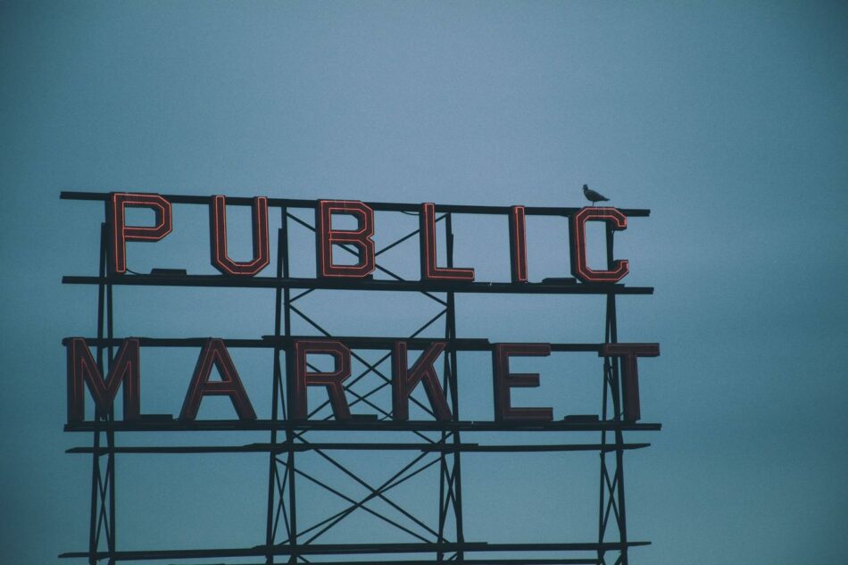 A bird sits on top of a public market sign.