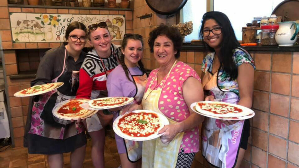 A group of women posing for a photo while holding plates of pizza.