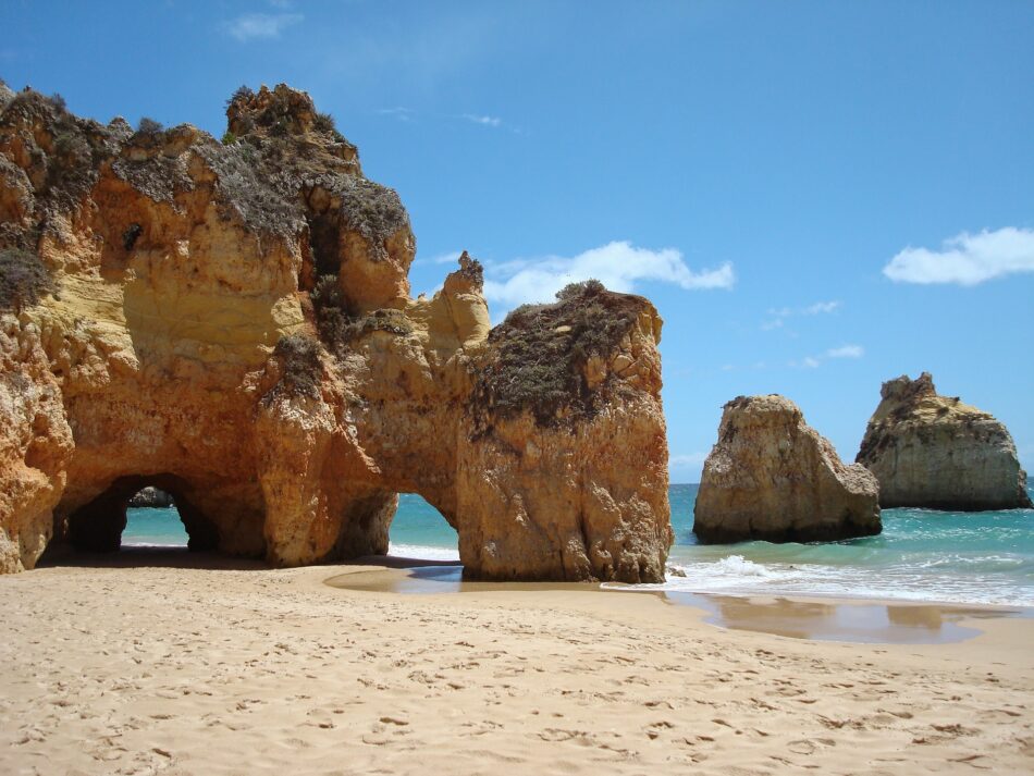 A sandy beach with rock formations in an affordable country to travel to.