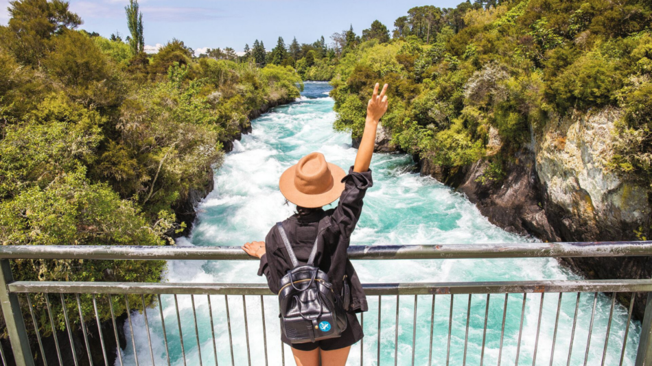 A woman is standing on a bridge overlooking a river in new zealand.