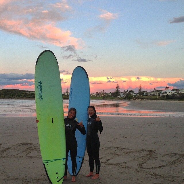 Two women standing on a surf spot beach with surfboards.