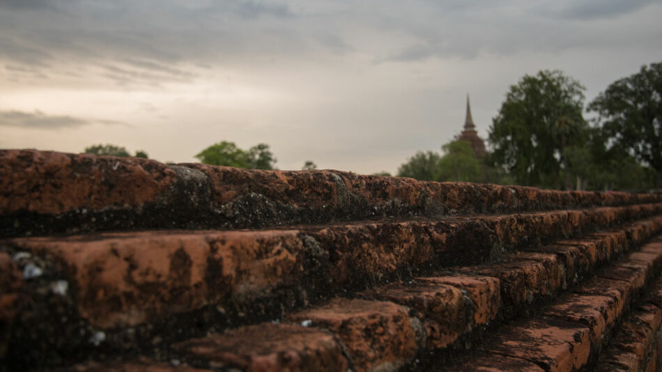 In one of the most beautiful destinations in Thailand, a brick wall stands tall with a serene steeple rising in the background.