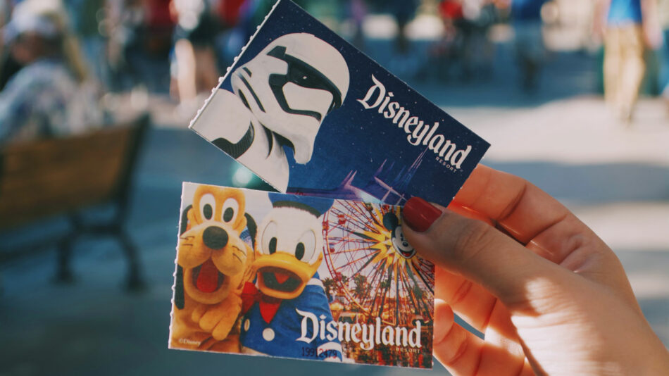 A person holding two disneyland tickets in front of a crowd.