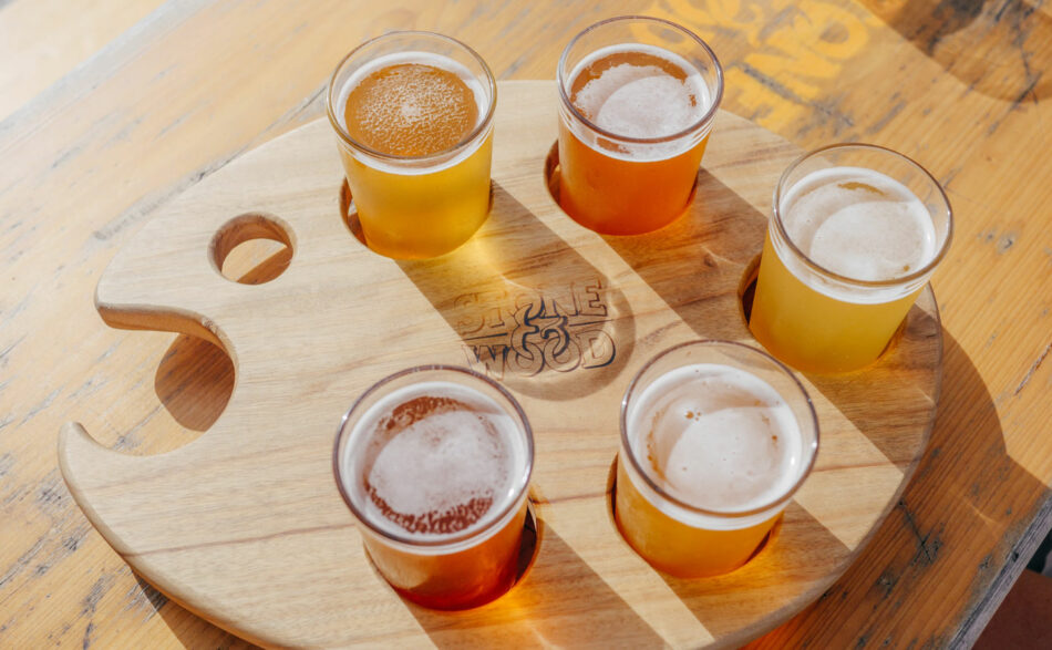 Five glasses of beer on a wooden tray.