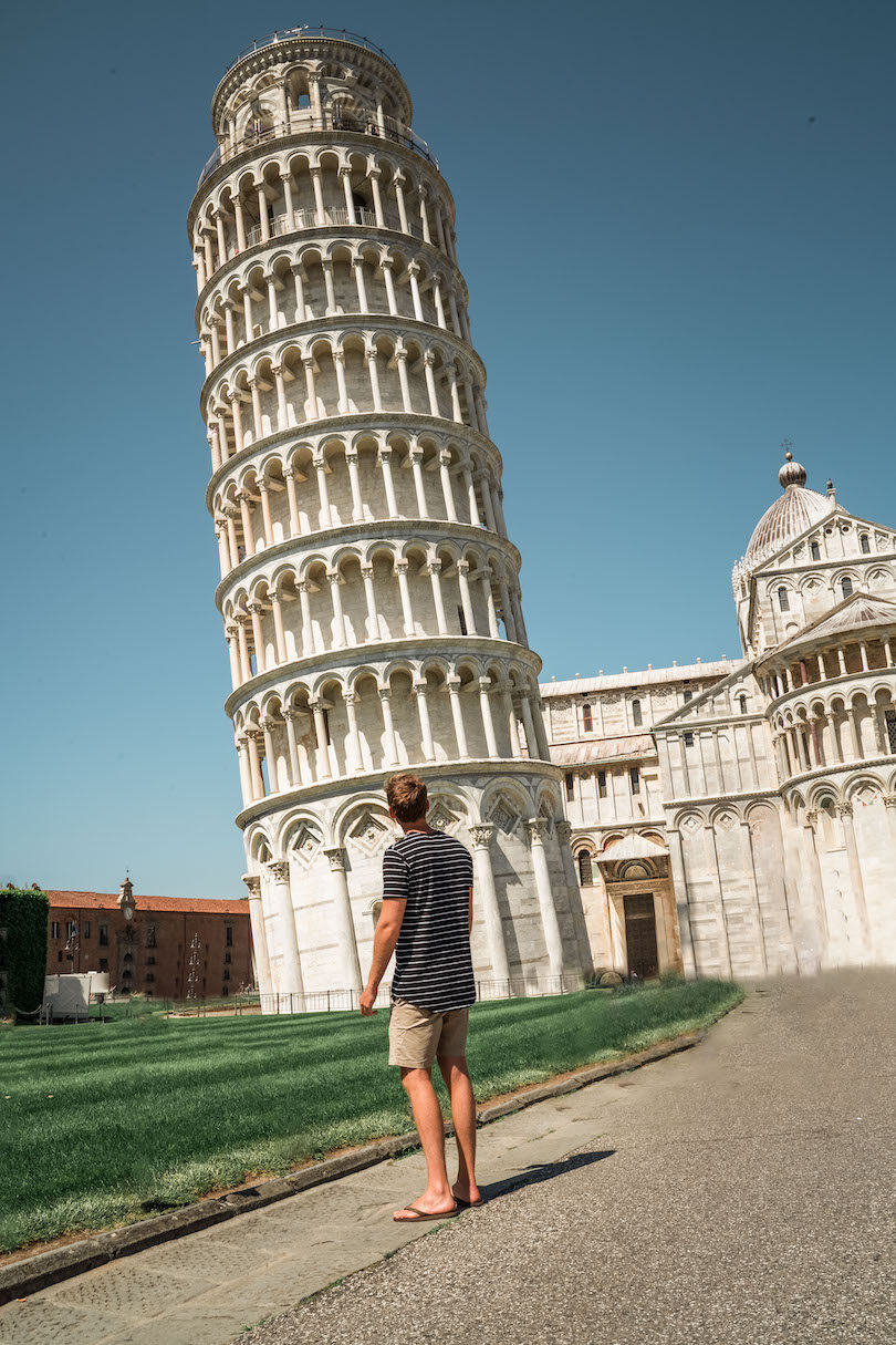 A man is standing in front of the leaning tower of pisa.