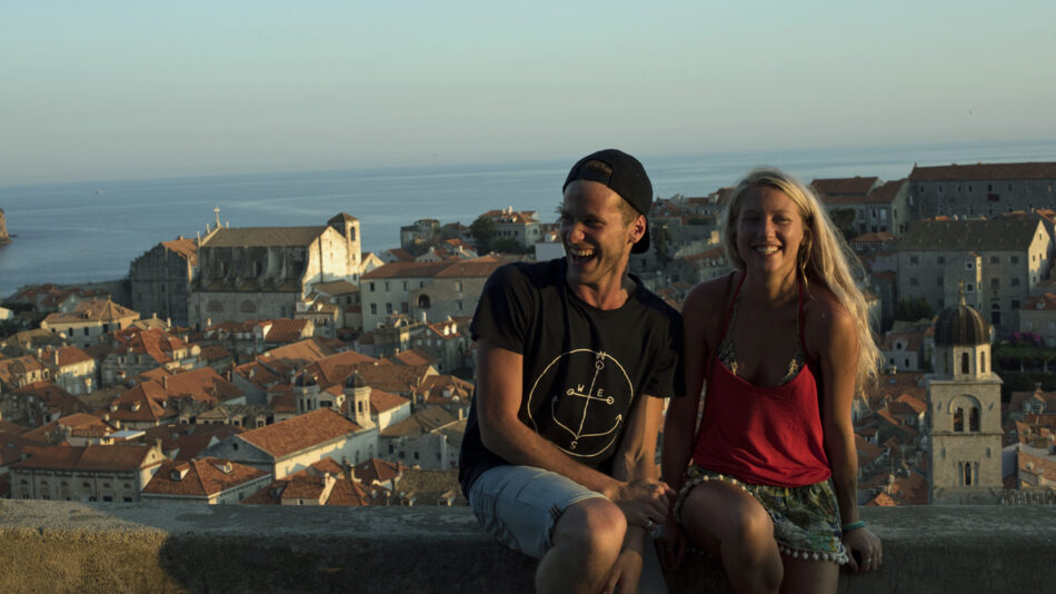 A couple traveling alone sits on a ledge overlooking the city of Dubrovnik.