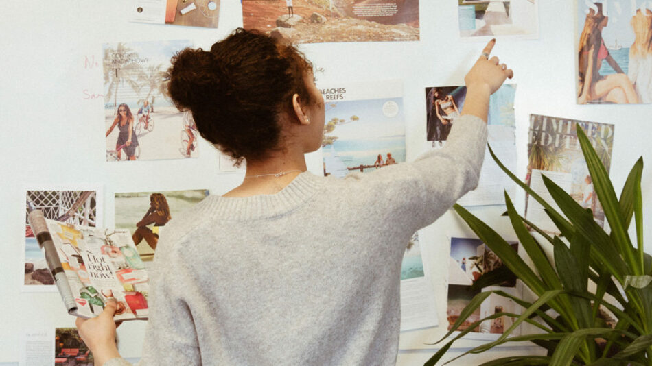 A woman exploring travel photos on a wall.