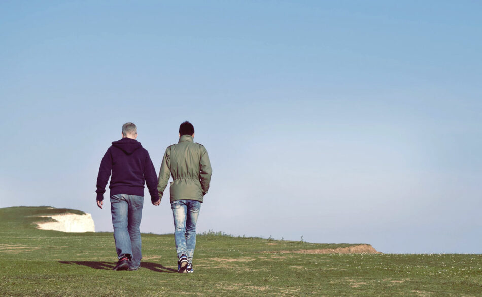 Two men find love while walking on a grassy hill.