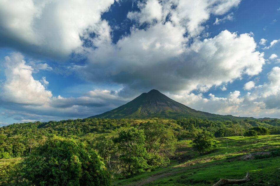 One of the best places to visit in Costa Rica is a picturesque mountain adorned with lush green grass and gently kissed by clouds in the background.