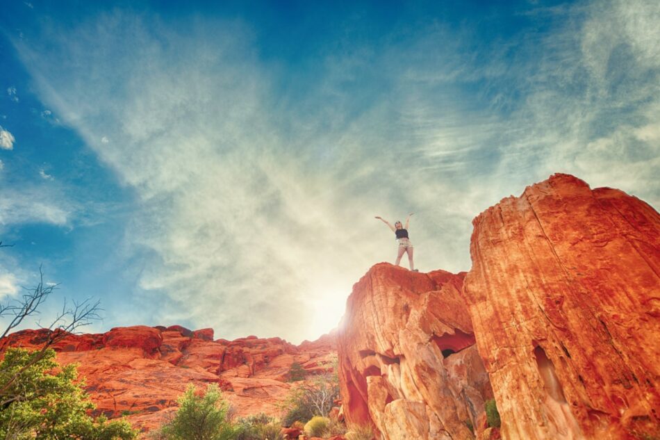 A woman is standing on top of a red rock.