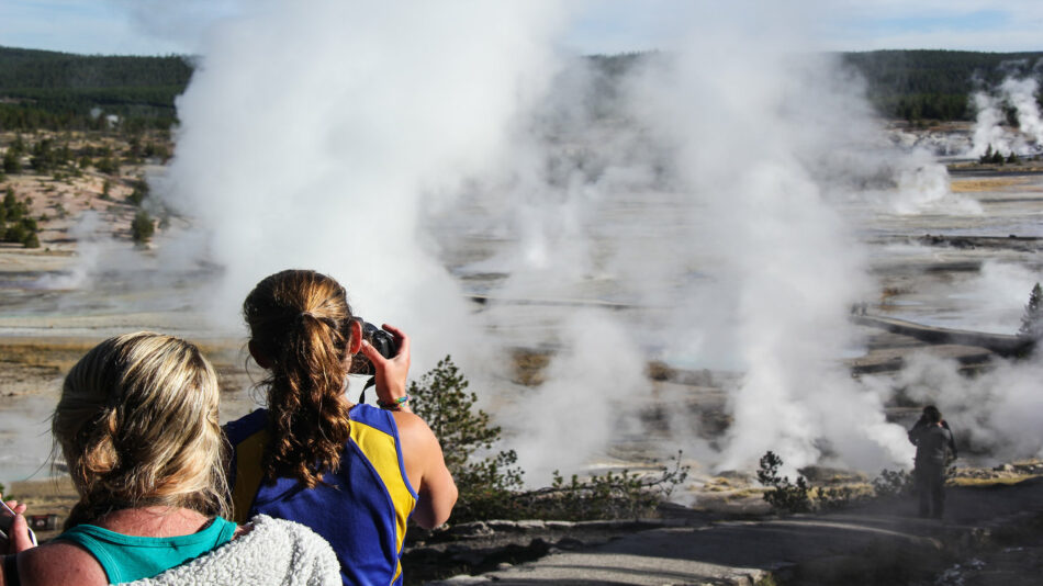 A group of people taking pictures of a geyser in yellowstone national park.