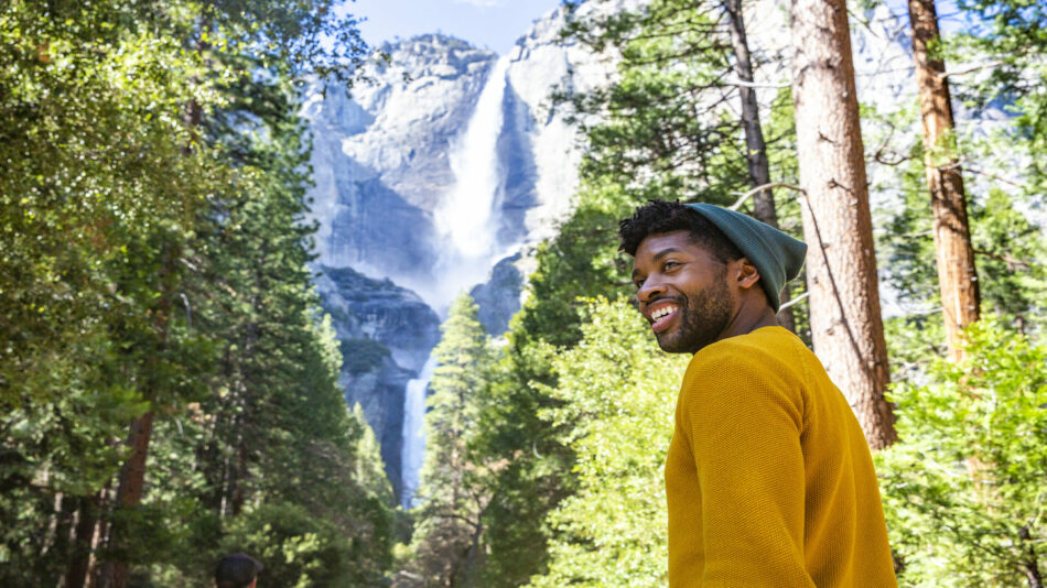 A man is standing in front of a waterfall in yosemite national park.