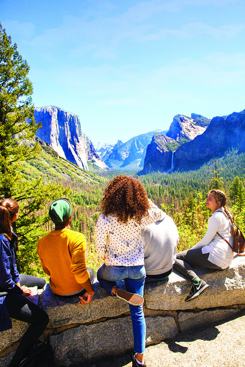 A group of people sitting on a ledge admiring one of the best national parks in the distance.