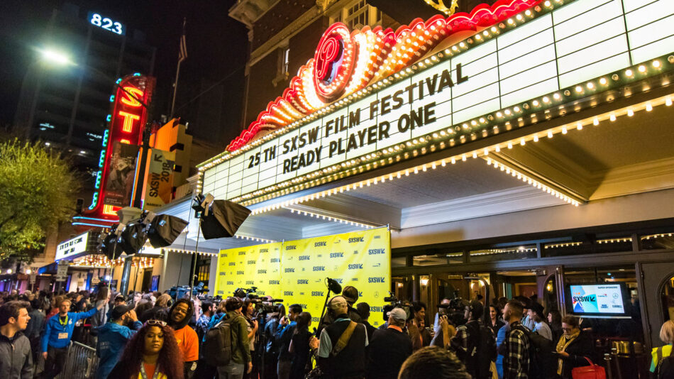 A crowd of people standing outside a theater at night, eagerly awaiting one of the best festivals in March.